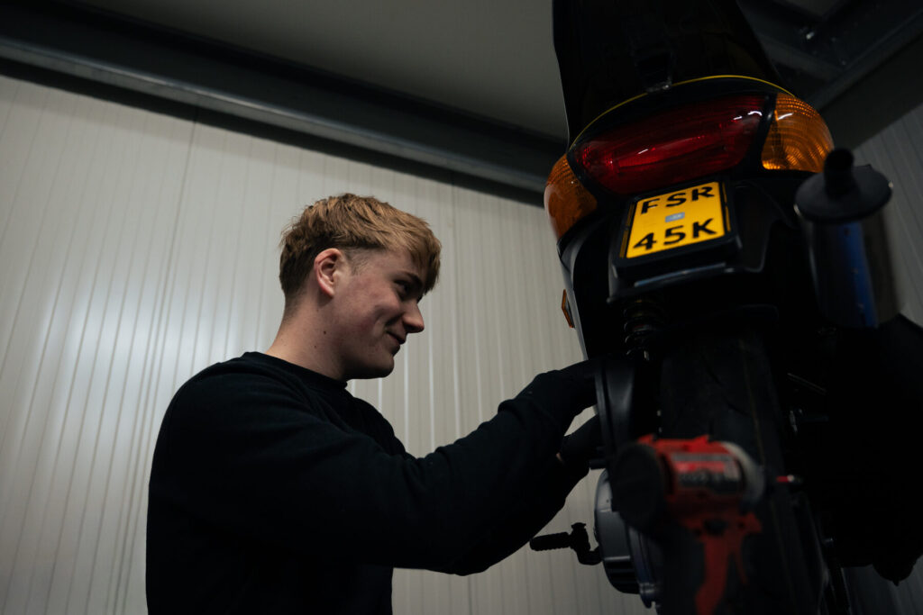 Monteur van Italian Classics 2 Wielers werkt aan het achterwiel van een scooter