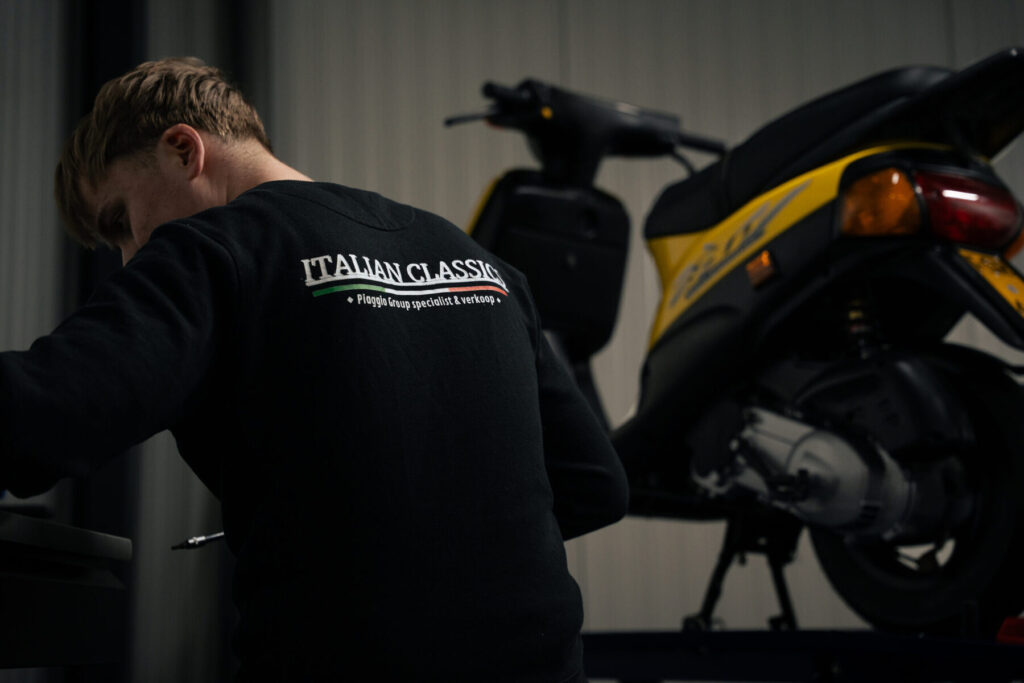 Monteur in Italian Classics trui aan het werk aan een gele Piaggio Zip